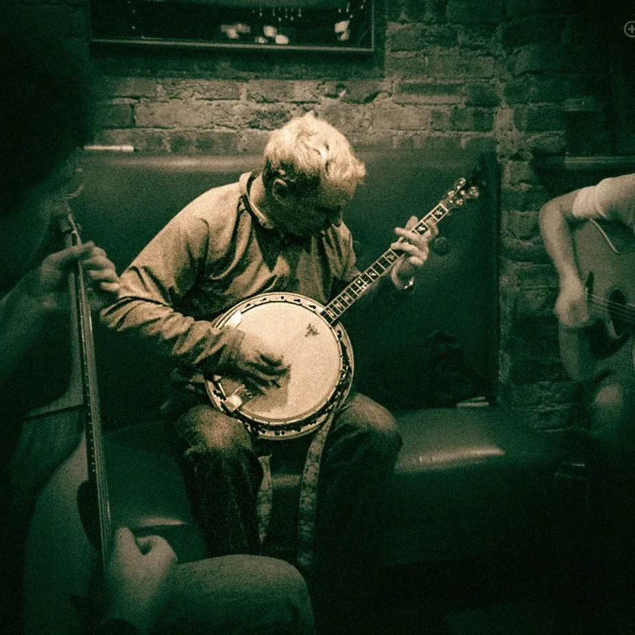 Three musicians play banjo, guitar, and bass in a dimly lit bar.