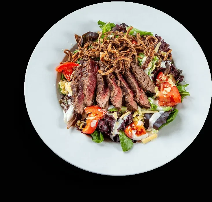 Close-up overhead shot of a steak salad with crispy onion strings.
