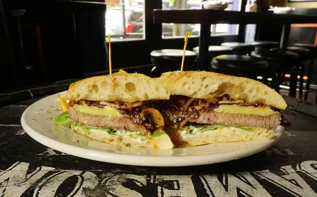 Large sandwich with steak, melted cheese, and vegetables on a plate.
