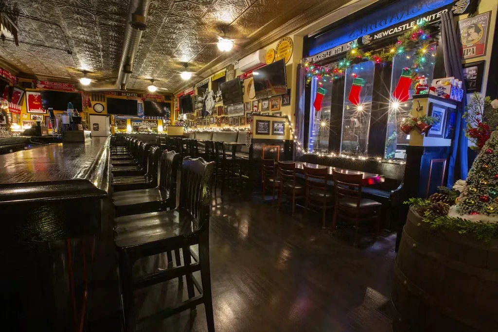 Warmly lit pub interior with a long bar and holiday decorations.