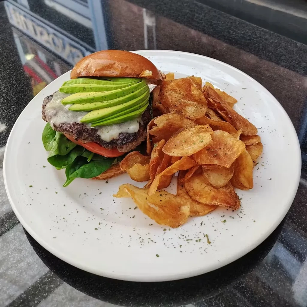 Gourmet burger with avocado, tomato, spinach, cheese, and potato chips.