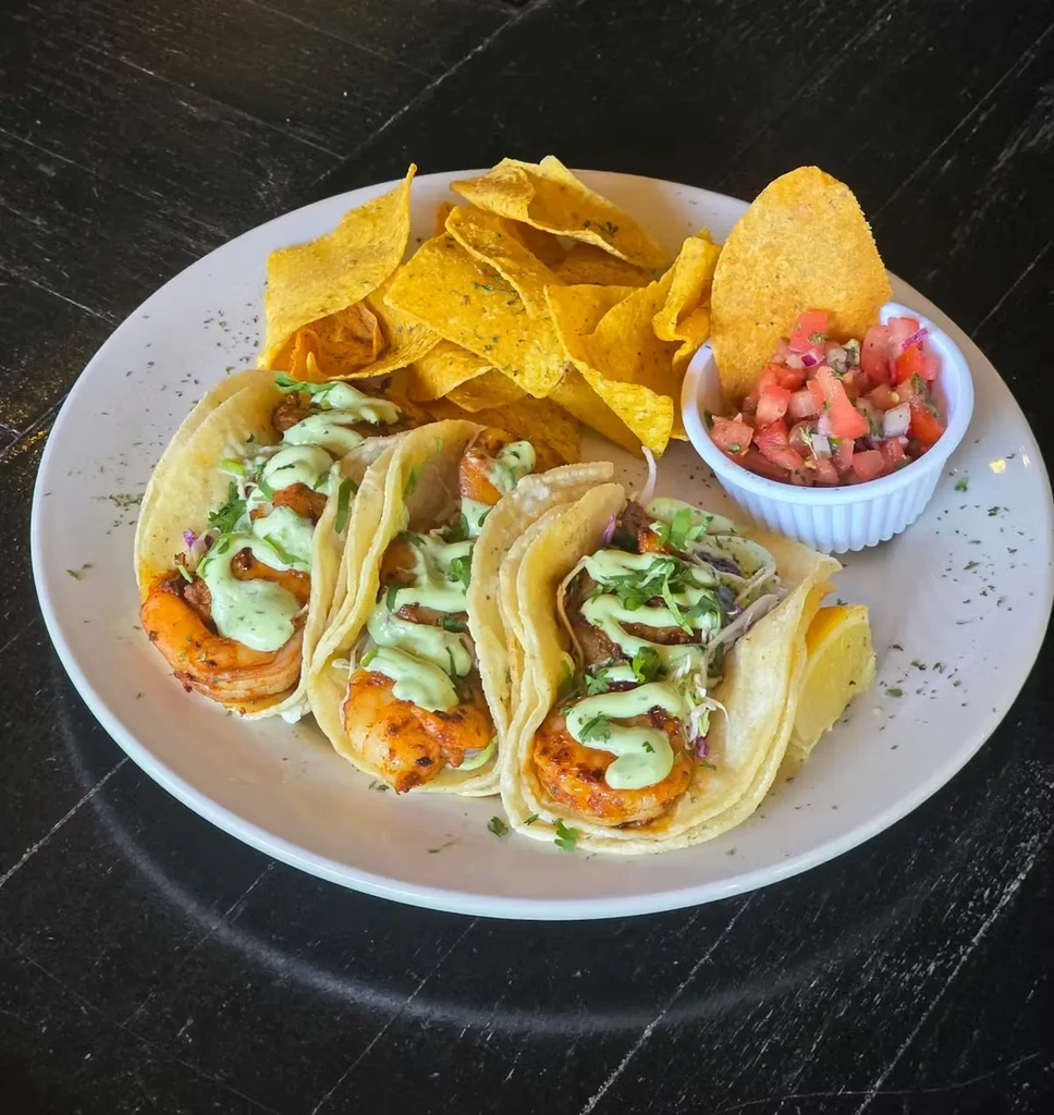 Three shrimp tacos with chips, pico de gallo, and lemon.