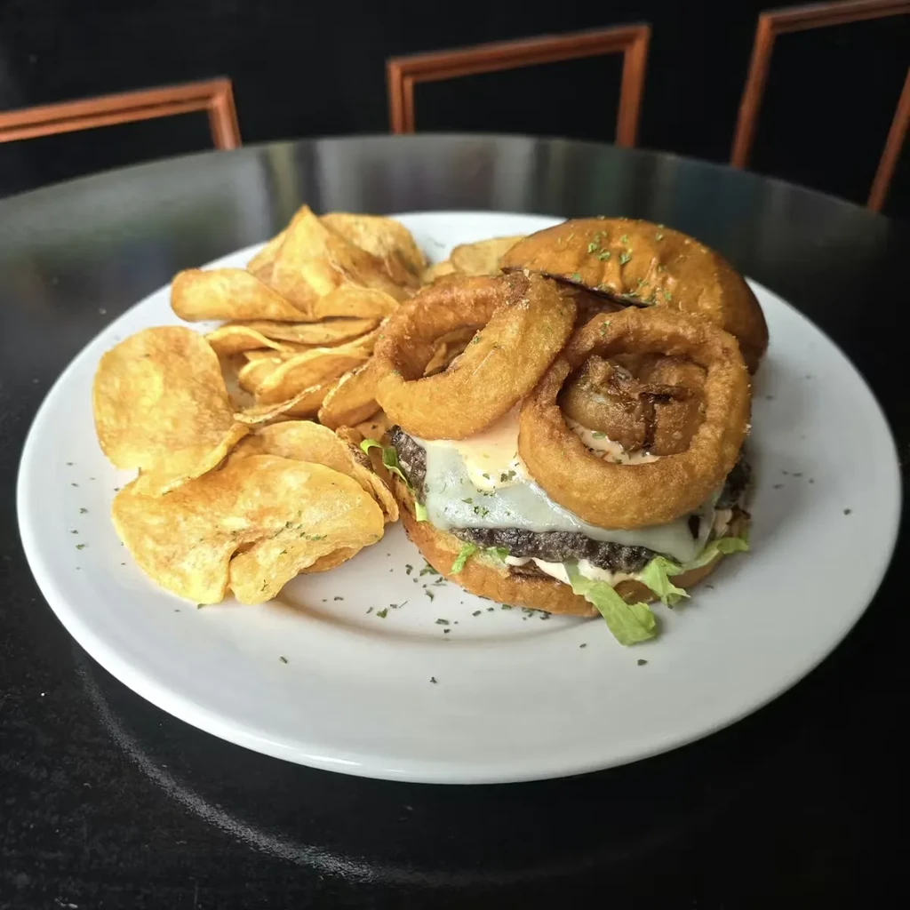 A burger with cheese and onion rings, chips, and parsley.