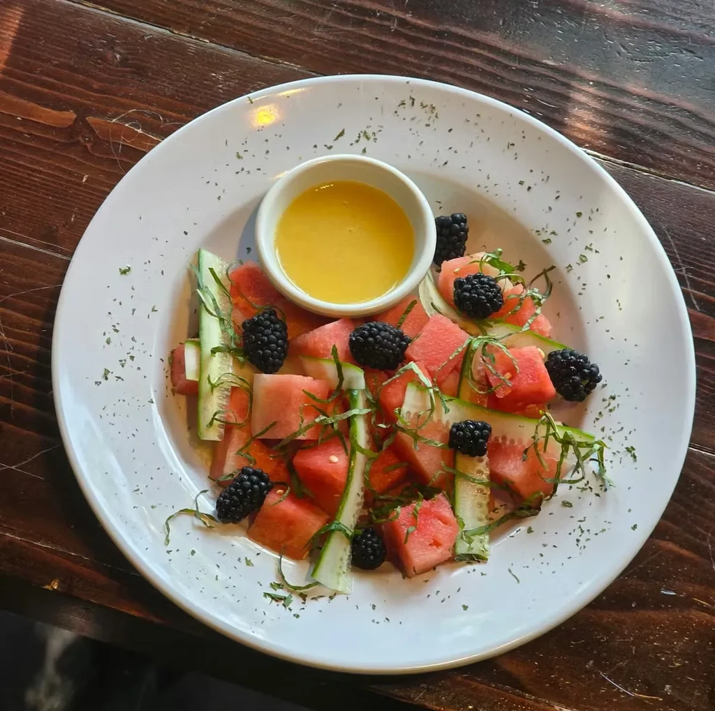 Fruit salad with watermelon, cucumber, blackberries, herbs, and yellow dressing.