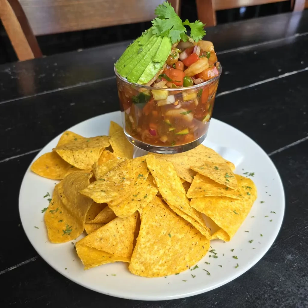 Ceviche in a glass, topped with avocado, served with tortilla chips.