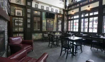 Cozy, empty restaurant interior with dark wood, red armchairs, and tables.