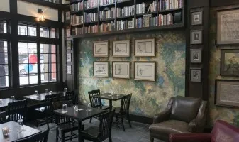 Restaurant interior with distressed walls, bookshelves, framed art, and tables.