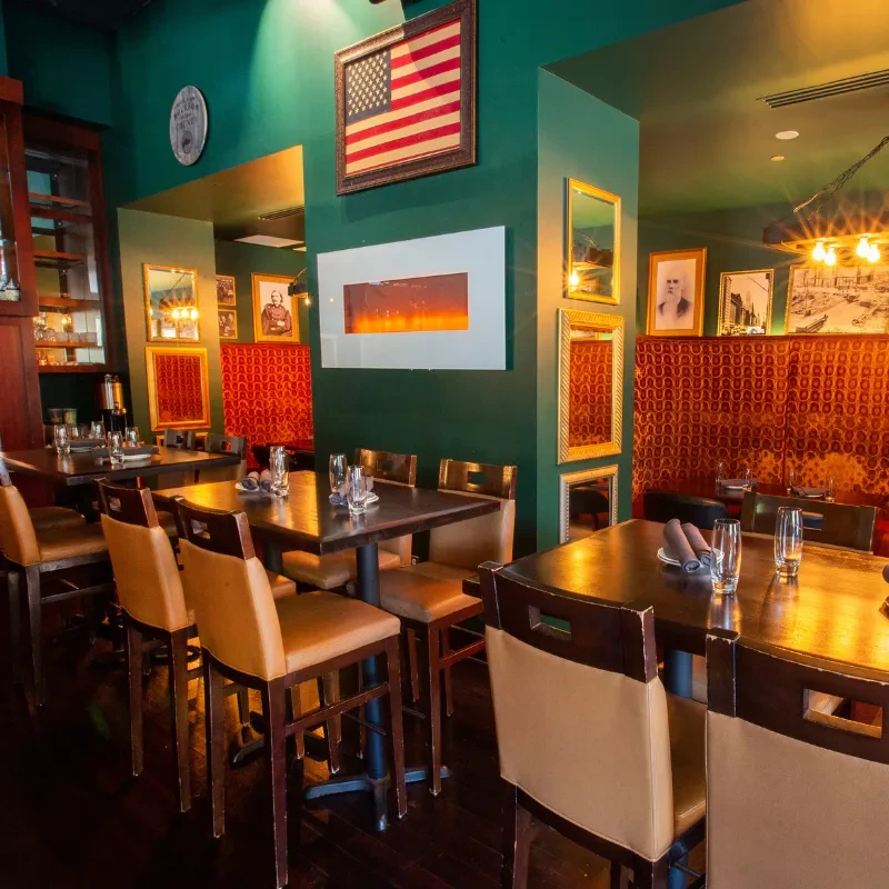 Restaurant interior with dark green walls, wood furniture, and framed art.