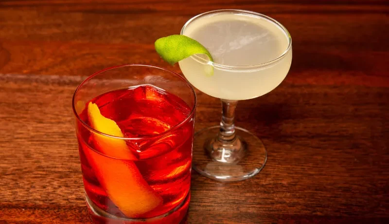 Two cocktails: a Negroni and a light-colored drink.