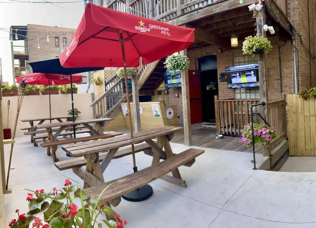 Outdoor patio with picnic tables, umbrellas, and hanging flower baskets.