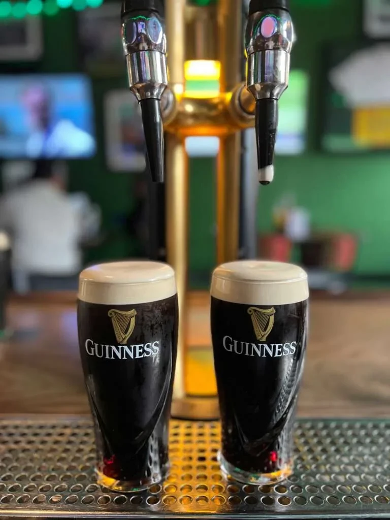 Two perfectly poured Guinness pints with creamy heads on a drip tray.