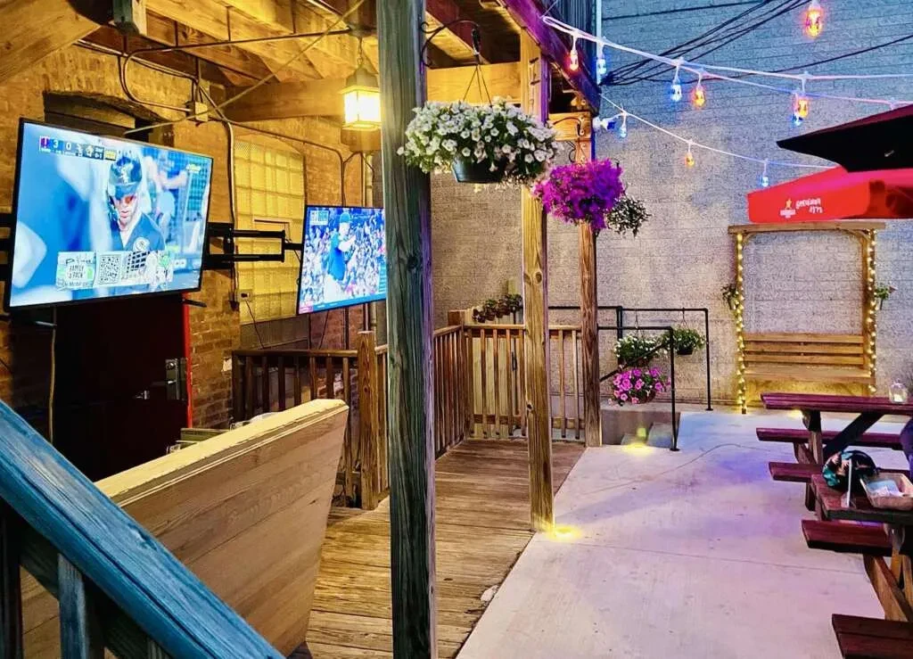 Outdoor restaurant patio with baseball on TVs, string lights, and picnic tables.