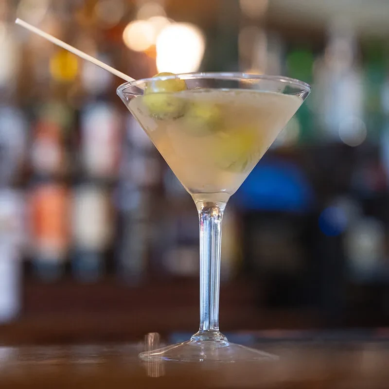 Martini glass with pale yellow drink and two green olives.