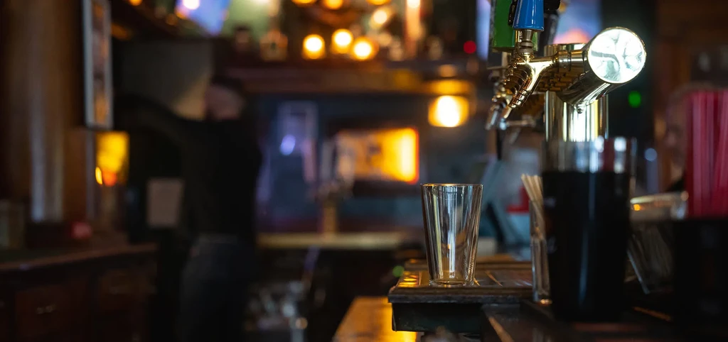 Metallic mixing glass on a bar mat in front of golden beer taps.