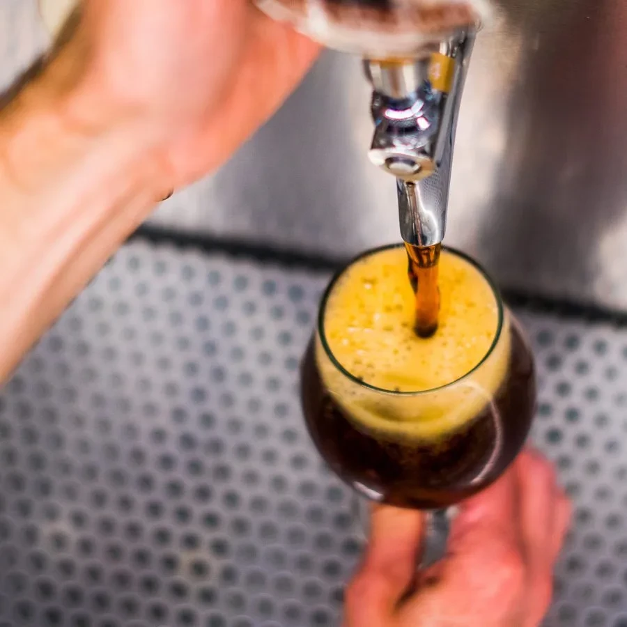 Hand filling stemmed glass with dark liquid from a tap.