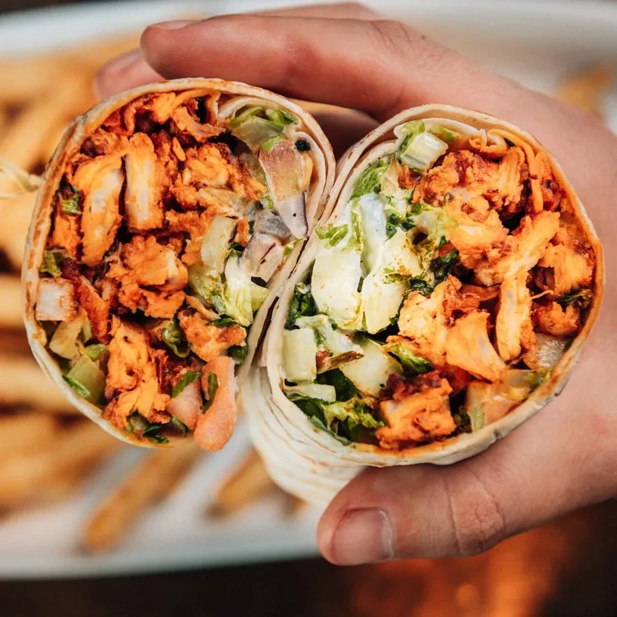 Hands hold a sliced wrap with chicken, lettuce, and white sauce.