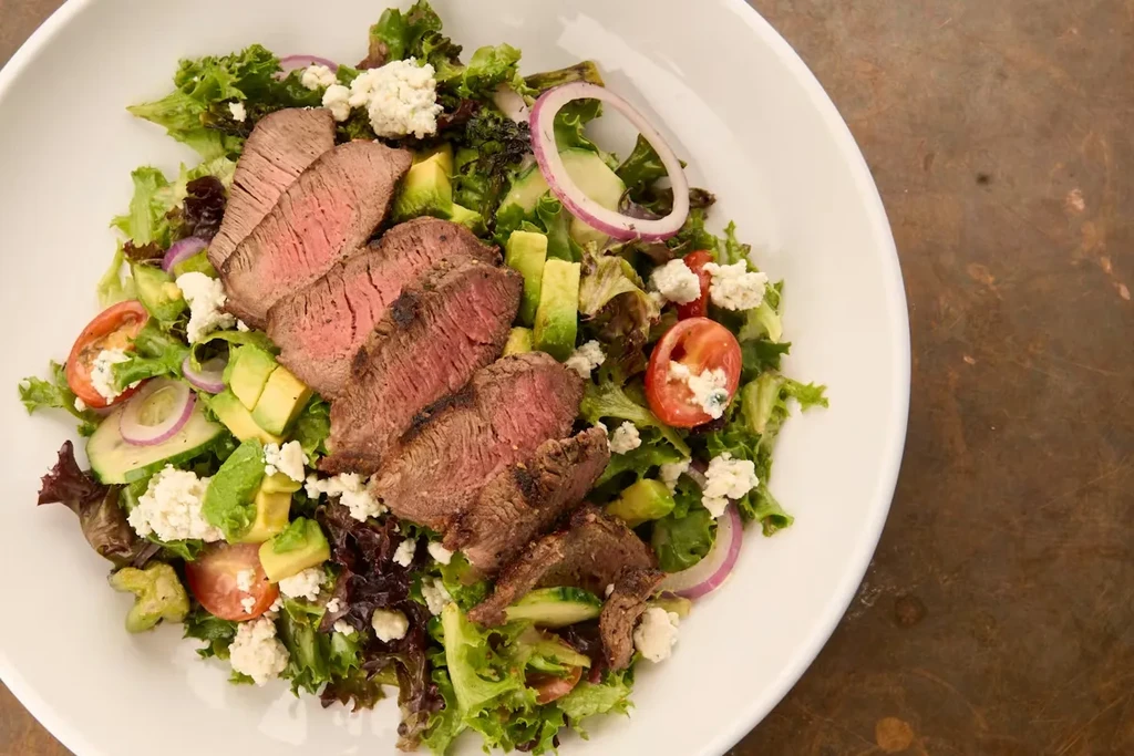 Grilled steak salad with avocado, tomatoes, red onion, and cheese.