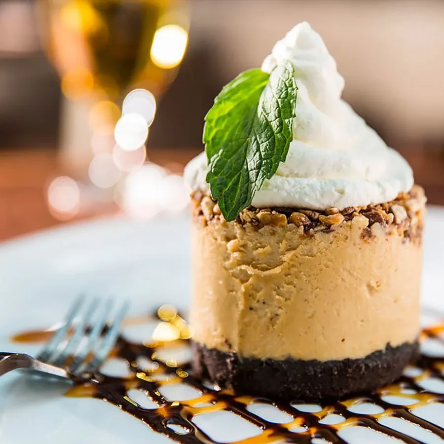 Cheesecake with whipped cream, nuts, and mint leaf on a plate.