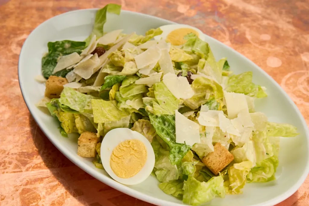 Caesar salad in a white dish, topped with cheese and egg.