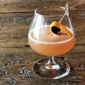 Amber cocktail in stemmed glass, garnished with orange peel.