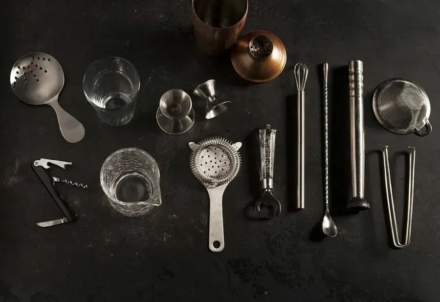 Flat lay of various bar tools and glassware on a dark surface.