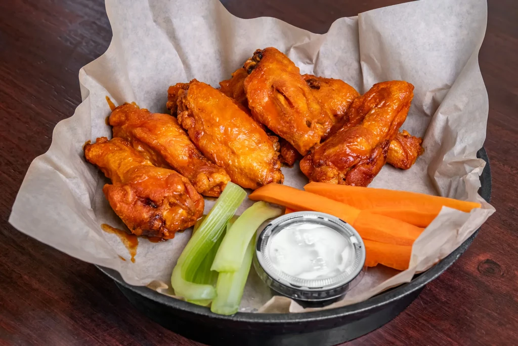 Buffalo wings in a cast iron skillet with celery and carrots.