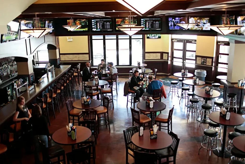 Spacious restaurant interior with diners, a long bar, and multiple TVs.
