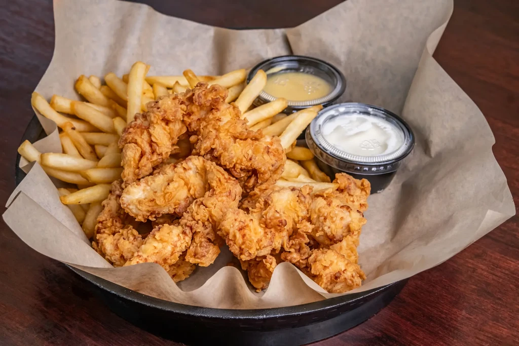 Fried chicken tenders and french fries in a basket with sauces.