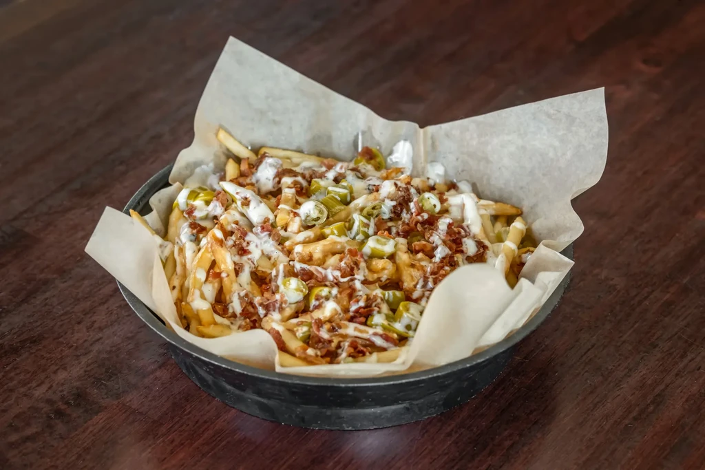 Loaded french fries in a black bowl on a wooden surface.