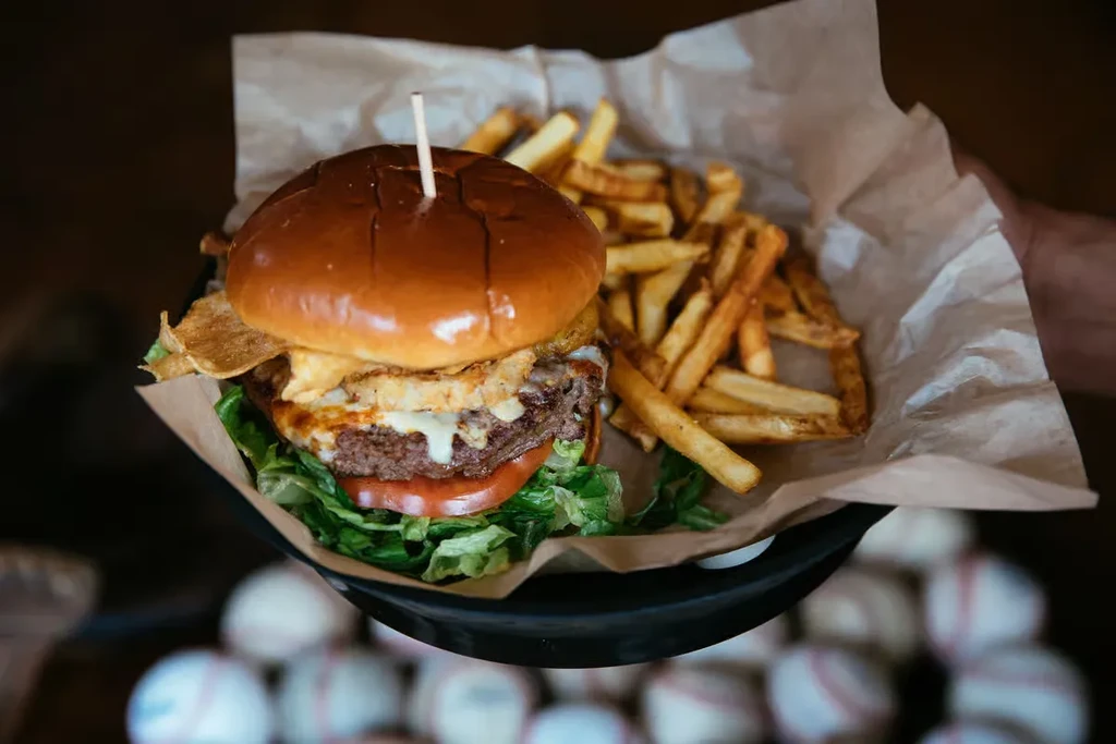 Gourmet burger and fries served in a bowl, baseballs in background.