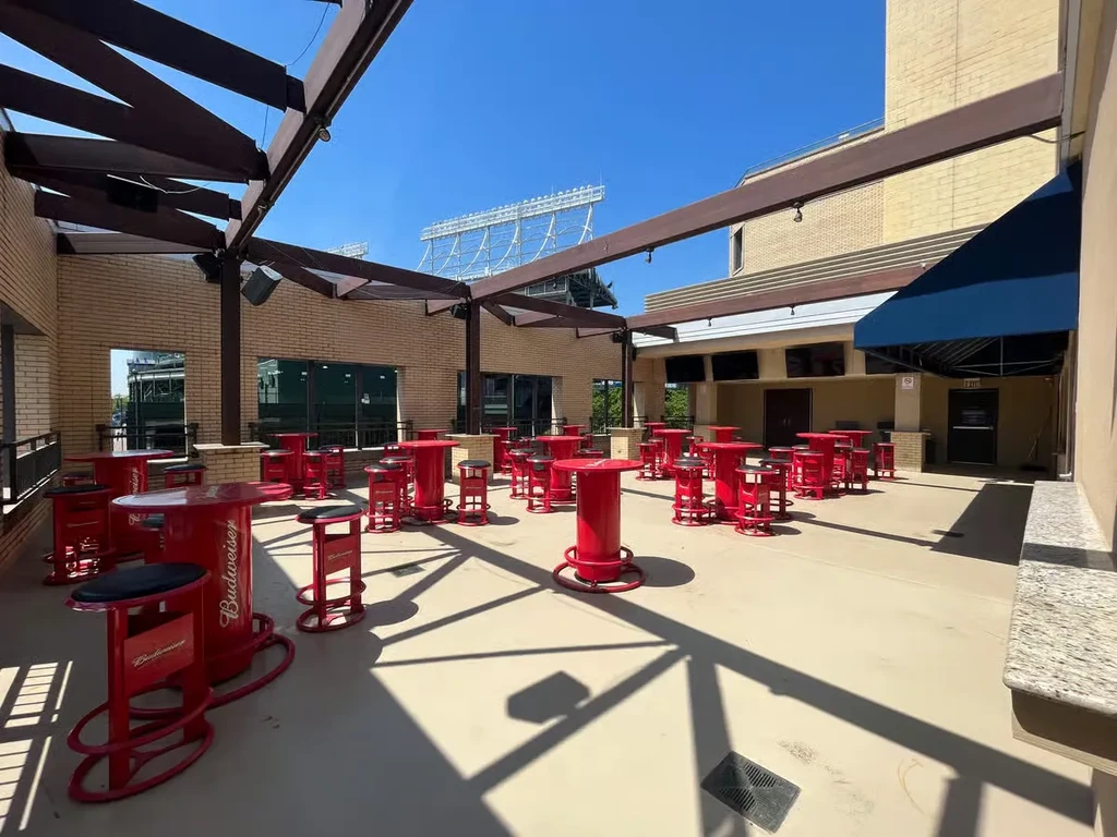 Outdoor patio with Budweiser high-top tables and stadium lights.