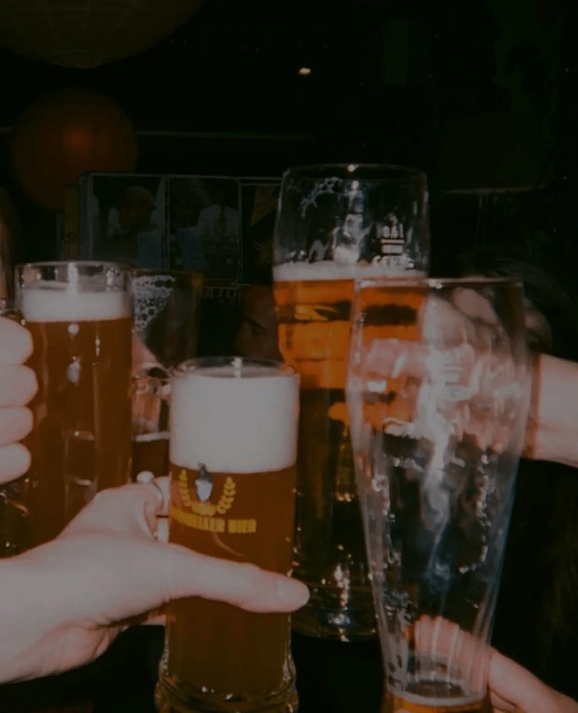 Group of people toasting with various beer glasses in a dim setting.