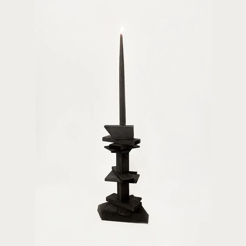 Black candle burning in an abstract, geometric black candlestick.