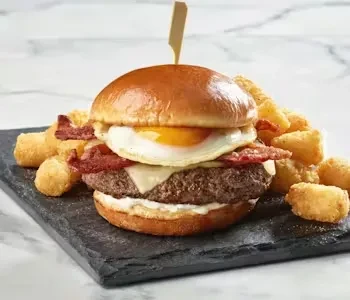 Gourmet burger with egg and bacon, tater tots on a slate plate.