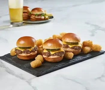 Three mini cheeseburgers and tater tots on a slate plate.