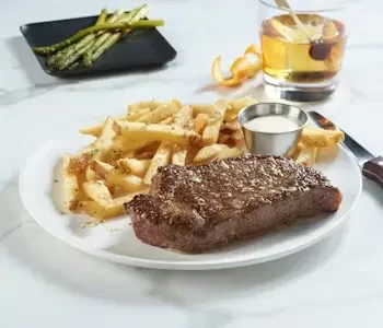 Grilled steak, french fries, asparagus, and a drink on a modern table.
