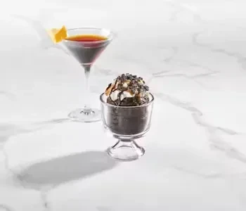 Dark cocktail with lemon, dessert with syrup and sprinkles.