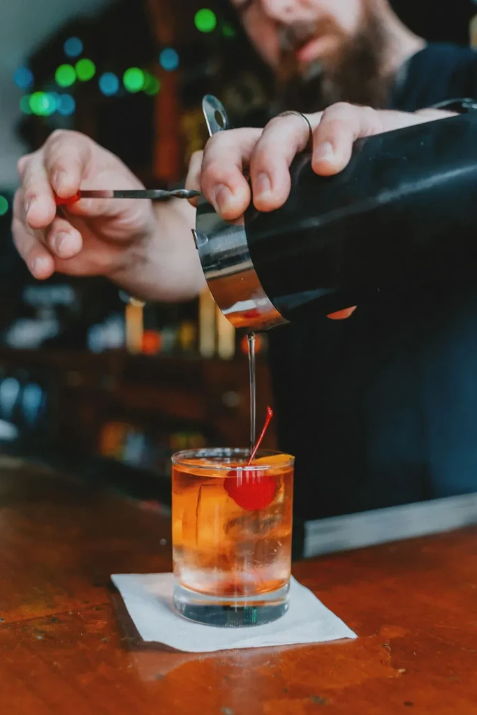 Bartender pours an amber drink into an Old Fashioned glass.