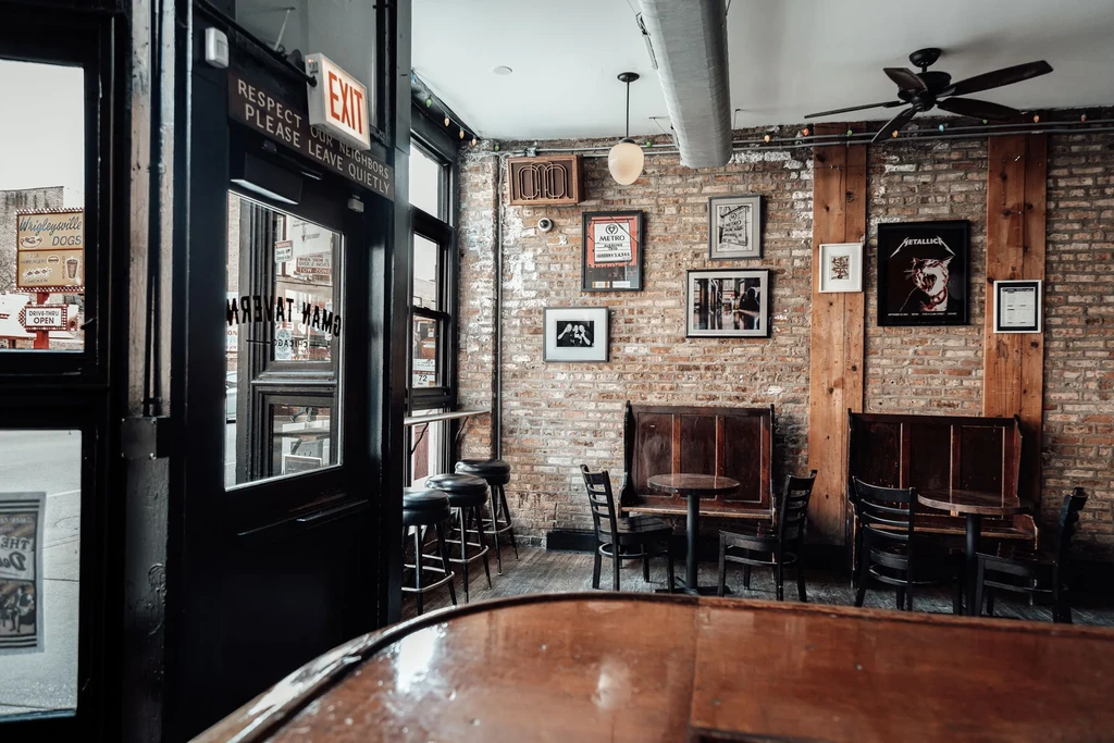 Rustic bar interior with exposed brick, framed art, and booth seating.