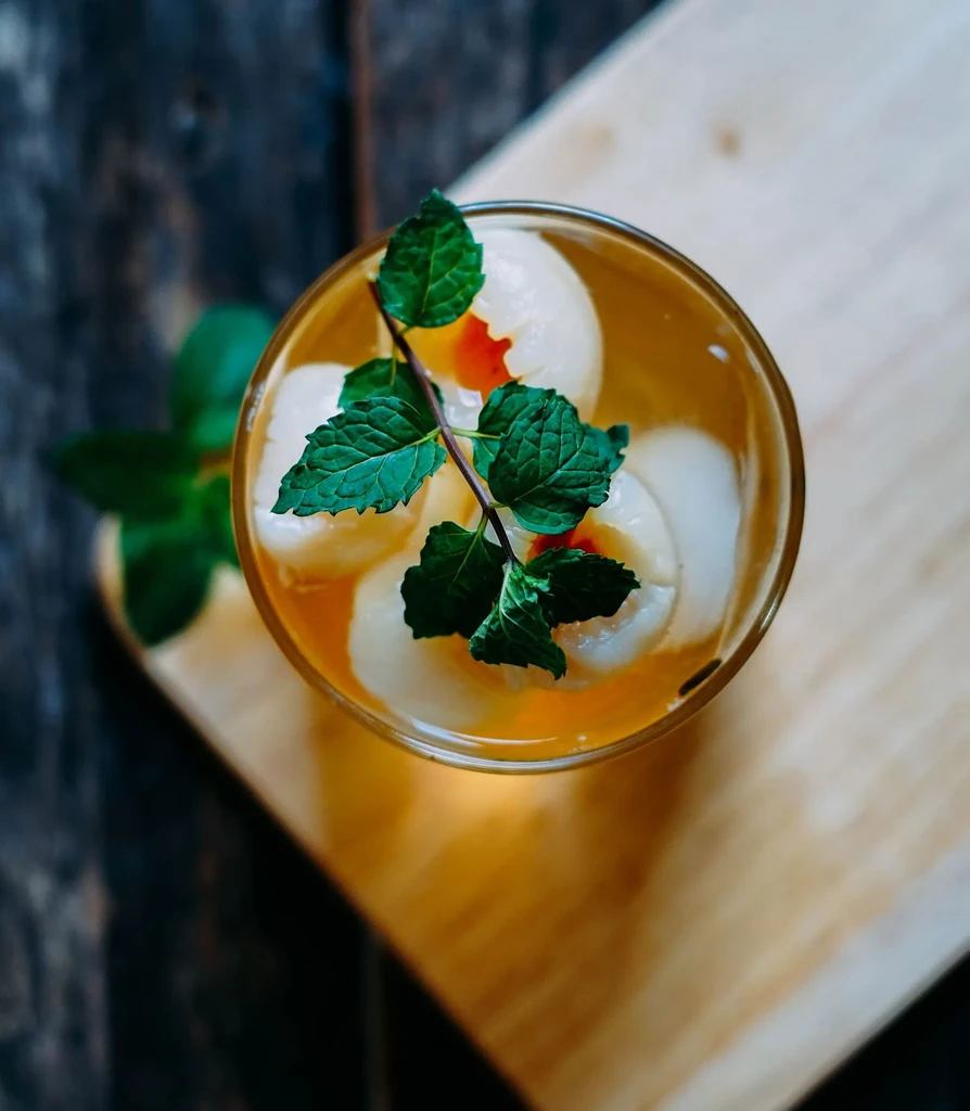 Overhead shot of clear glass with amber drink, fruit, and mint.