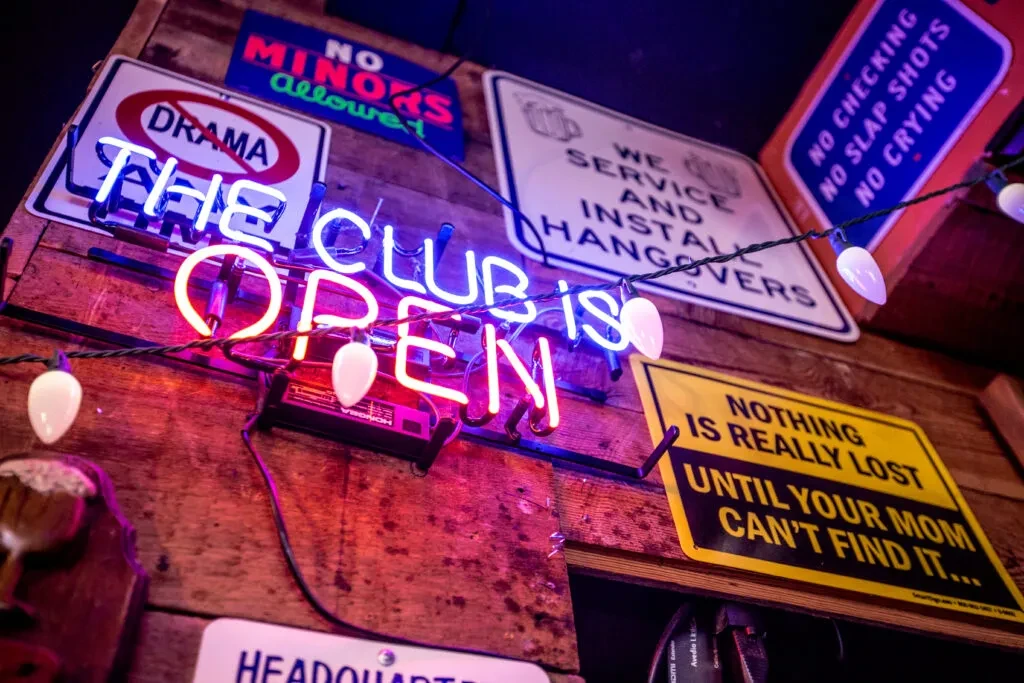 Neon signs and lightbulbs on a rustic wooden wall.