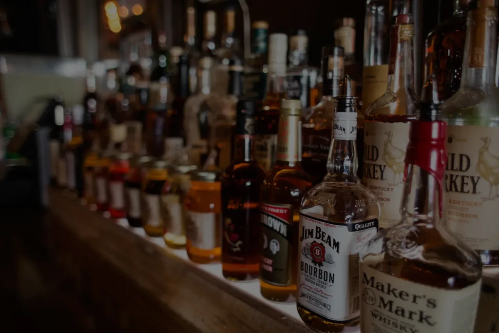 Whiskey and bourbon bottles with pour spouts on a bar counter.