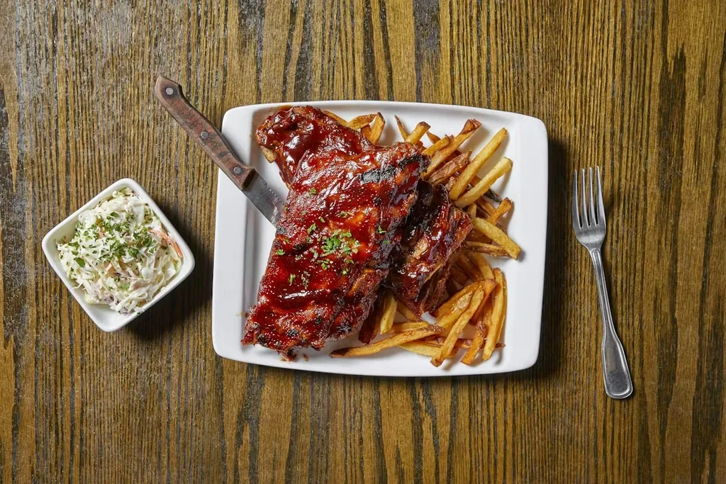 Rack of BBQ ribs, french fries, and coleslaw on a wooden table.