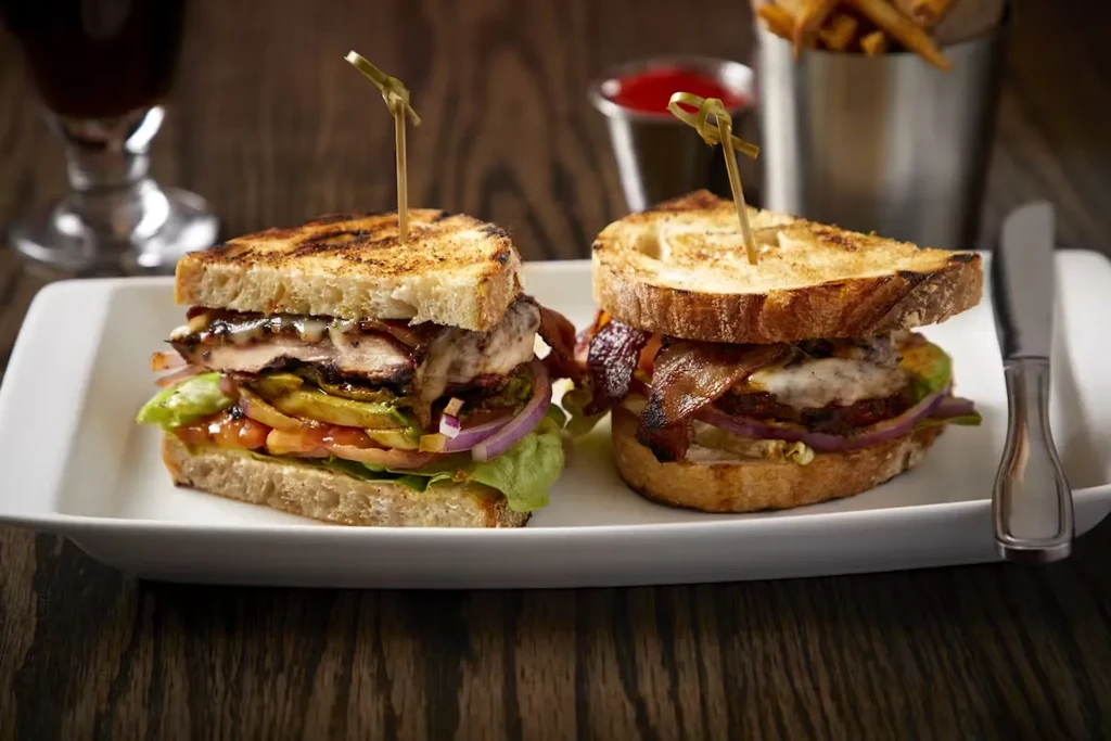 Two gourmet sandwiches on a white plate with fries and a drink.