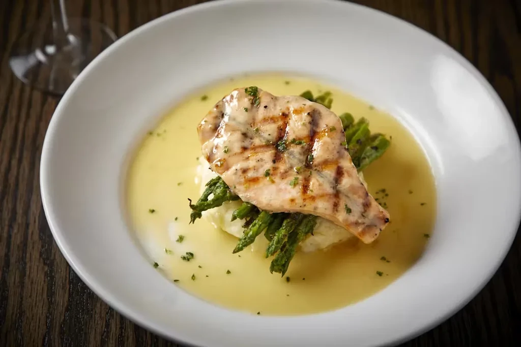 Grilled fish with asparagus, mashed potatoes, and sauce in a white bowl.