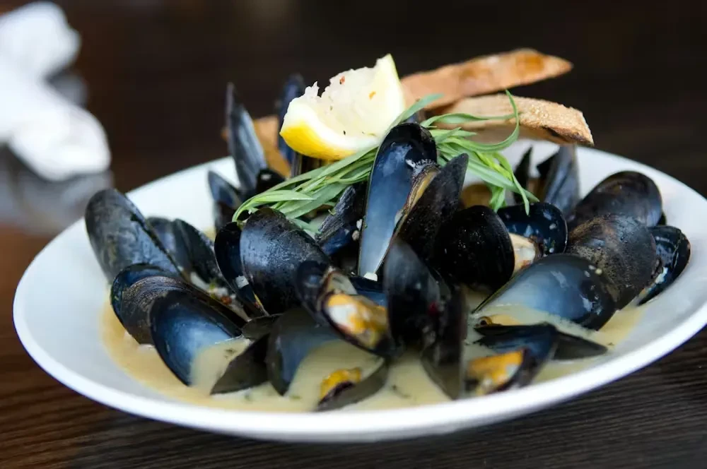 Close-up of mussels in cream sauce, lemon wedge, and green herbs.
