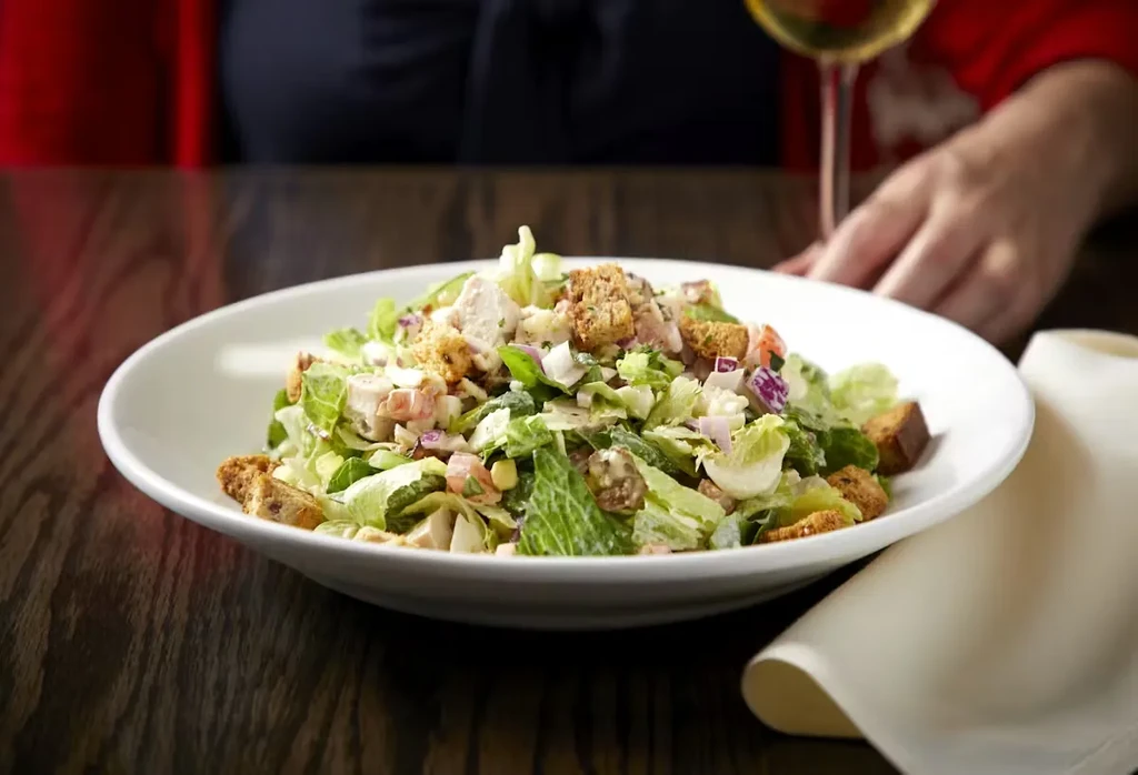 Close-up of a Caesar salad with chicken, croutons, and red onion.