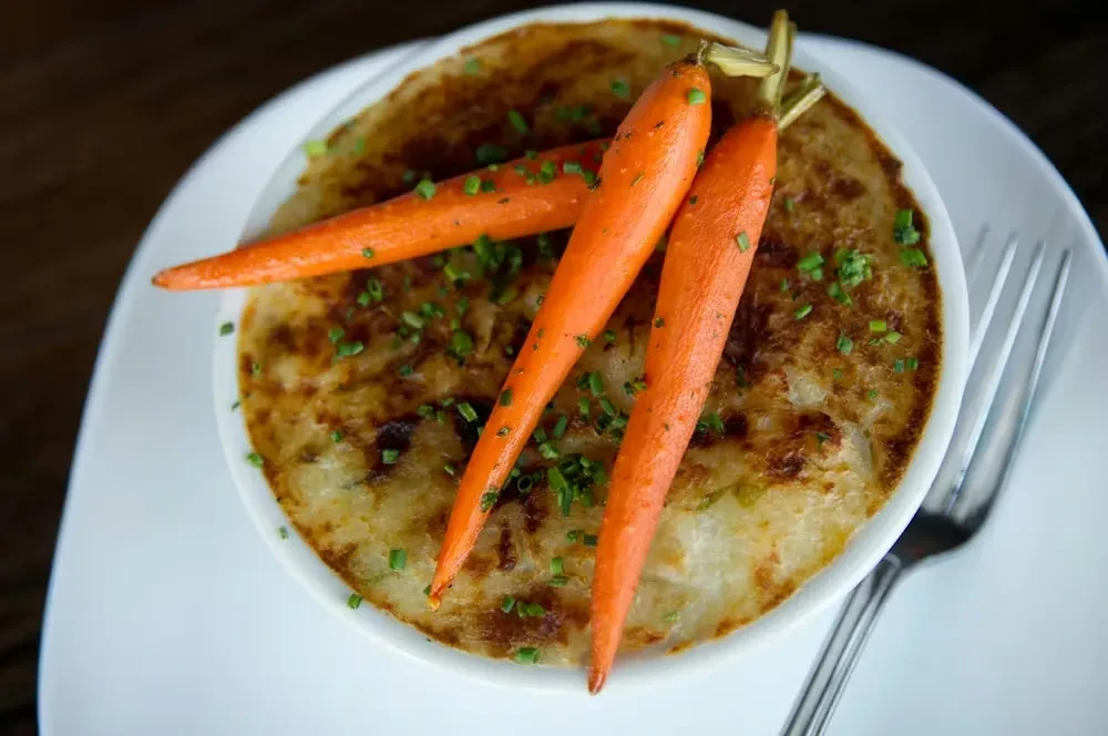 Creamy baked dish topped with roasted carrots and green herbs.