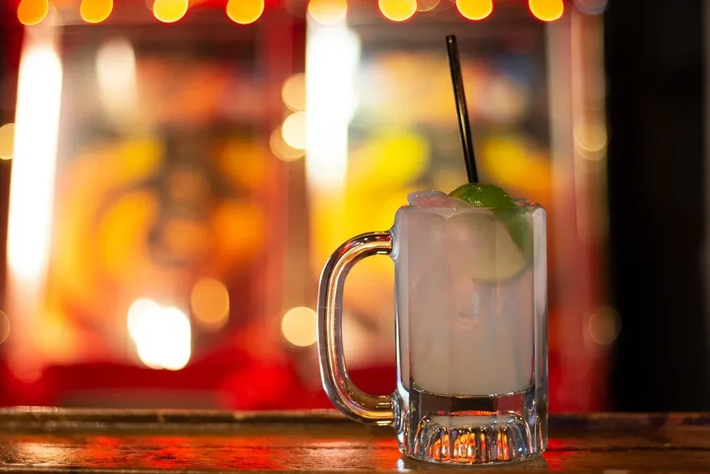 Ribbed glass mug with a drink, ice, lime, and black straw.