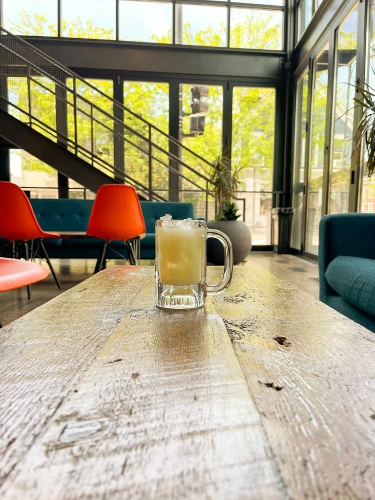 Mug with pale yellow beverage and ice on a wooden table.